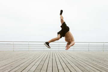 Muscular man doing a head jump upside down without touching his hands to the floor on the beach
