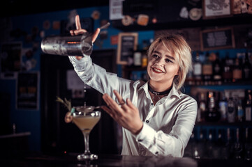 Pretty girl bartender adds ingredients to a cocktail behind bar