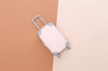 Travel minimalism. Mini plastic travel suitcase on beige brown background. Minimal style. Top view, flat lay