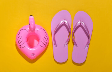 Inflatable pink flamingo with flip flops on yellow sunny background. Summer, beach vacation concept. Minimalism. Top view.