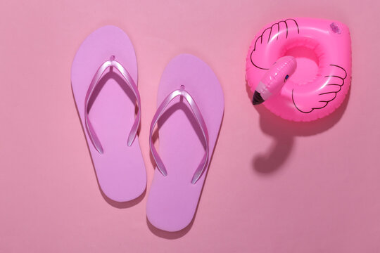 Inflatable pink flamingo with flip flops on pink sunny background. Summer, beach vacation concept. Minimalism. Top view.