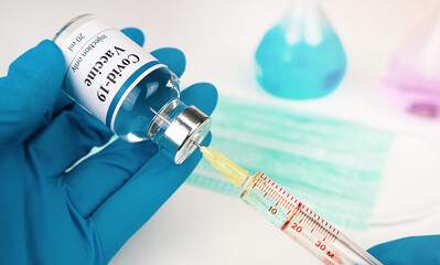 Doctor's hand holds a syringe and a blue vaccine covid19 bottle at the hospital. 