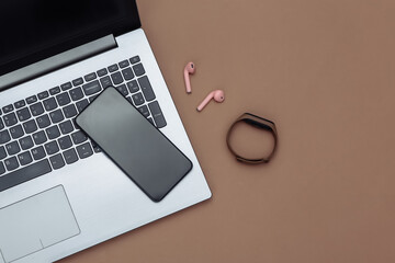 Laptop, smartphone, Wireless headphones and smart bracelet on brown background. Modern gadgets. Top view