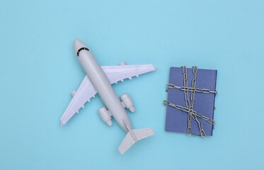 Passport wrapped in a metal chain and air plane on blue background. Travel ban. Top view