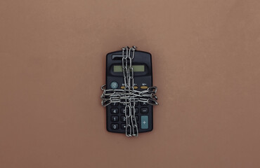Calculator wrapped in steel chain on a brown background. Top view