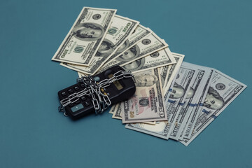 Calculator wrapped in steel chain and hundred dollar bills on blue background