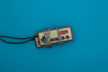 Retro joysticks wrapped in a chain on a blue background. Top view. Video game addiction