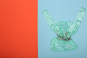 Cellophane bag wrapped in steel chain on blue orange  background. Copy space. Top view