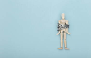 Wooden puppet wrapped in steel chain on blue background. Deprivation of liberty, confinement. Top...