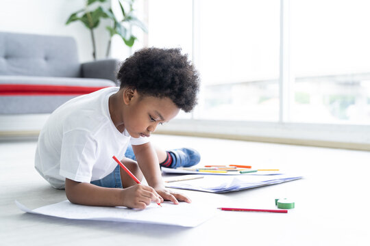 African American little boy drawing on pages with colour pencils on floor at home. kid, learning and education concept