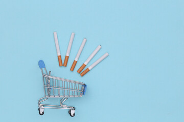 Shopping cart with cigarettes on a blue background. Top view