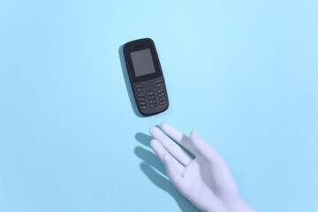 Mannequin's hand holds a push-button telephone on blue background. Top view
