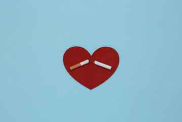 The harm of smoking to the heart. Heart with broken cigarette on blue background. Quitting smoking
