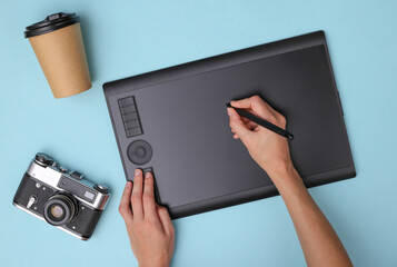 Woman photographer or retoucher working with graphic tablet on blue background. Top view