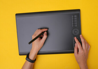 Woman graphic designer or retoucher working with graphic tablet on yellow background. Top view