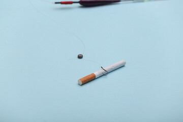 Nicotine addiction concept. Cigarette on the hook of a fishing rod on a blue background