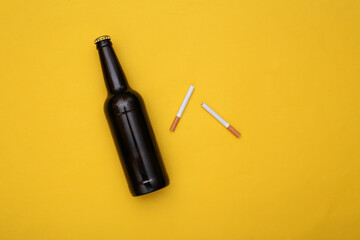 Naklejka premium Beer bottle and cigarette on yellow background. Alcohol and nicotine addiction