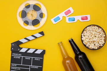 Movie time. Popcorn, film reel, beer bottles, movie clapper, 3d glasses on yellow background. Top view. Flat lay