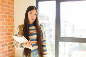 young asian woman feeling puzzled and confused, with a dumb, stunned expression looking at...