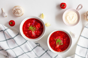 Top view of the traditional Ukrainian borscht or soup with beets, potatoes, tomatoes, meat in bowls on a white background. Top view, copy space.