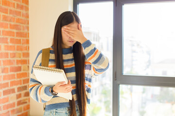 young asian woman covering face with hand and putting other hand up front to stop camera, refusing...