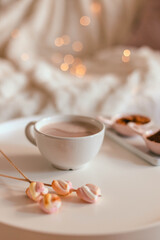 Ceramic cup of hot chocolate or cocoa with marshmallow on a white table. Decoration garlands of lights. Autumn and winter holidays