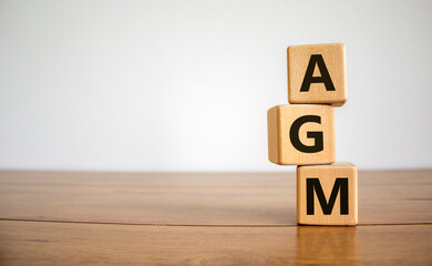 Wood cubes with acronym 'AGM' - 'annual general meeting' on a beautiful wooden table, white...