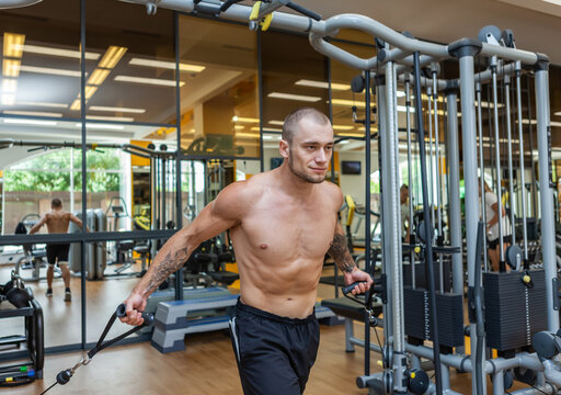 Muscular bodybuilder with naked torso exercises in cable crossovers machine. Fitness men pumping up muscles in gym.