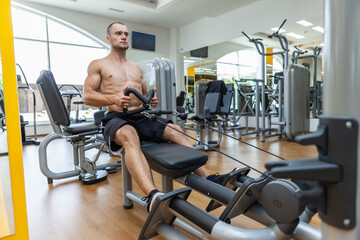 Naklejka na ściany i meble Fitness muscular man with a naked torso working out rowing cable machine. Back workout