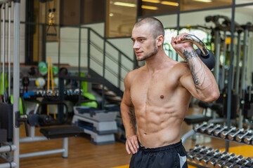 Workout-focused muscular sculpted man exercising with a kettlebell in modern gym. Bodybuilding strength training