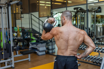 Naklejka premium Workout-focused muscular sculpted man exercising with a kettlebell in modern gym. Bodybuilding strength training