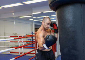 Muscular man with a naked torso in boxing gloves boxing a punching bag