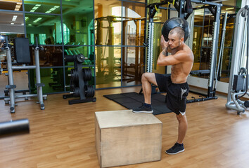 Obraz na płótnie Canvas Muscular fitness man is pacing on a wooden box with medicine ball on his shoulder in the gym. Cross training