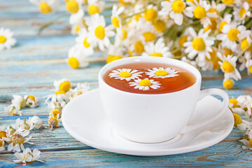 Daisy flowers in a white cup of tea, chamomile herbs on wooden background. Herbal medicine. Healthy lifestyle concept.