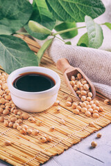 Soy sauce with soya beans scattered on a bamboo napkin against the background of burlap and branch young green pods soybean, closeup with selective focus