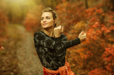 Young attractive sport woman in sportswear doing stretching exercise for hand in autumn forest with reddened leaves of trees. Warm up before training. Healthy lifestyle concept