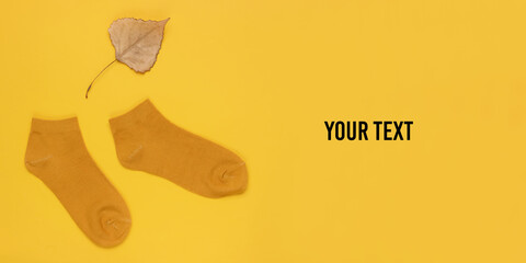 Autumn time. Orange socks with a dry fallen leaf on a yellow background with space for your text. Top view