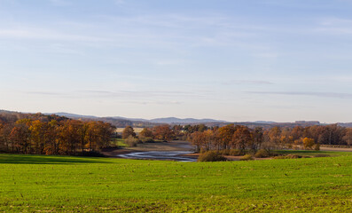 Fototapeta na wymiar Czech autumn landscape. Dry pond Dehtar with meadow, trees and distant hill at day time