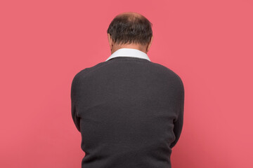 Mature man turning back to camera feeling alone. Studio shot on pink wall.