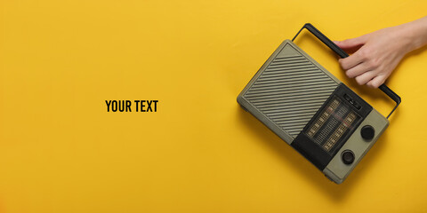 Female hand holds a retro radio receiver on a yellow background with space for your text. Retro...