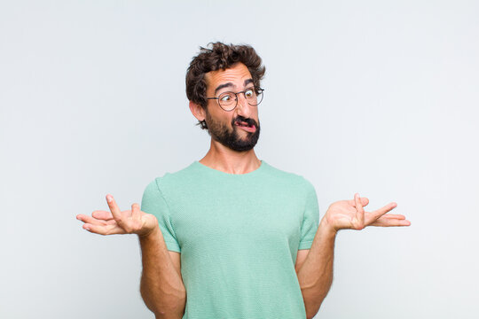 young bearded man shrugging with a dumb, crazy, confused, puzzled expression, feeling annoyed and clueless