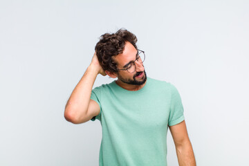 young bearded man smiling cheerfully and casually, taking hand to head with a positive, happy and...