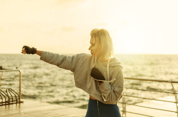 Young woman kickboxer with wrapped hands in bandages trains punch on the beach at sunrise. Morning...