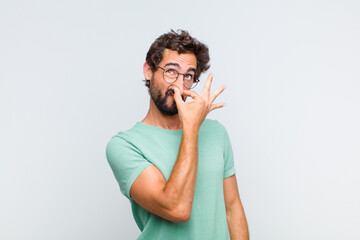 young bearded man feeling disgusted, holding nose to avoid smelling a foul and unpleasant stench