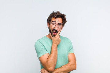young bearded man with mouth and eyes wide open and hand on chin, feeling unpleasantly shocked,...