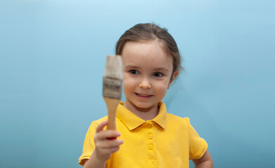 Little girl in a yellow T-shirt on a blue background. The child holds a brush in his hands.
