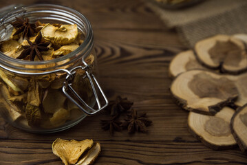 Homemade crispy sun dried organic apple slices. Close up of apple chips with spice in glass jar on brown wooden background with copy space for text
