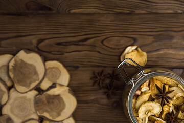 Homemade crispy sun dried organic apple slices. Close up of apple chips with spice in glass jar on brown wooden background with copy space for text
