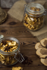 Fototapeta na wymiar Homemade crispy sun dried organic apple slices. Close up of apple chips with spice in glass jar on brown wooden background with copy space for text 