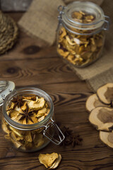 Homemade crispy sun dried organic apple slices. Close up of apple chips with spice in glass jar on brown wooden background with copy space for text
